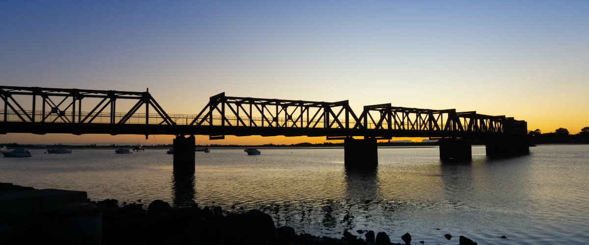 Silhouette of a Tauranga harbour bridge at sunset over still water — The Gold House® silver bullion products, New Zealand